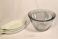 Photo showing three white ceramic serving or casserole dishes stacked together next to three clear heavy glass nesting bowls, total six items in the lot.