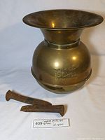 Full view of brass spittoon with two rusty rail spikes laid beside it, includes label identifying items.