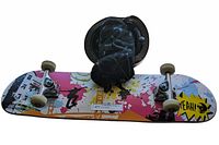 Photo of the skateboard showing colorful deck design with black helmet and protective pads on top.