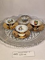 Photo showing all four teacup and saucer sets arranged on the large crystal serving tray, all cups have gold rims and interiors depicting different city or landmark designs.