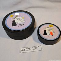 Two round black ceramic boxes with Instant Diva champagne themed labels, containing plates and coasters, placed on a white surface.