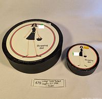 Photo showing two round boxes with labels indicating 'Shopping Girl Plates' and 'Coasters' for Santa Barbara Ceramic Design.