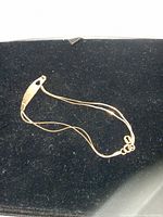 Photo of the full slender double chain gold bracelet with heart-shaped central plate on a black display background.