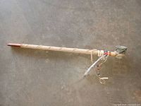 Full view of the peace pipe laying flat on a concrete floor, showing the soapstone bowl, leather wrapping and long wooden stem.