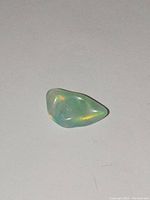 Polished natural flame opal showing aqua blue and teal green color flashes on a plain white background.
