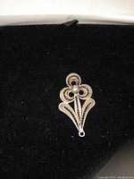 Silver flower charm or pendant with filigree design on a black velvet background, showing the front side with spherical bead center and loop attachment.