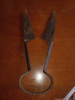Pair of antique iron sheep clippers shown on wooden surface, displaying their triangular blades and loop handles.
