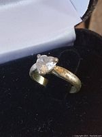 Front angle of ring showing heart-shaped clear topaz stone set in gold-tone band with visible wear and peeling plating.