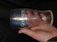 Clear Guinness pint glass held in hand showing logo and typical pint shape.
