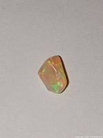 Polished freeform freestanding fire opal with orange base and vibrant green and red fire colors visible under light.