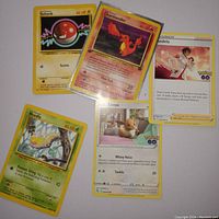 Photo showing five assorted Pokémon cards laid out on a surface including Voltorb, Charmander, Eevee, Weedle, and Mandela Trainer cards with visible text and artwork.