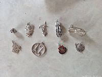 Overview of 9 sterling silver jewelry pieces including assorted charms and a brooch, laid out on a neutral surface.