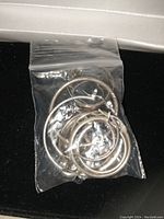 Plastic bag containing multiple mixed sterling silver earrings, various sizes of hoops visible, some with clasps, slightly tarnished.