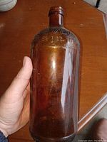 Photo showing the full amber glass bottle held in hand, highlighting the size, shape, and amber color with embossed volume measurements near the top
