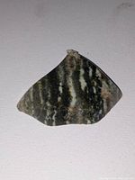 Polished and faceted granite specimen showing striped natural pattern, angled edges, and smooth surface on light background.