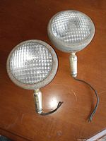 Pair of vintage automobile fog lamps on wood surface showing overall condition and wiring.