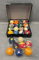 24 billiard balls arranged in a black box with white circle pattern, showing assortment of colors and patterns