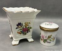 Side view of square footed planter with floral motif and gold scalloped rim alongside small floral trinket box with lid