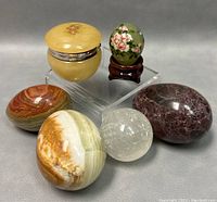 Five polished stone eggs, a hand painted Chinese mini egg on wooden stand, and a small decorated trinket box arranged on a grey background