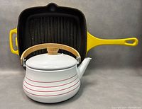 White enamel kettle with wooden handle and red stripes in front of the grill pan.