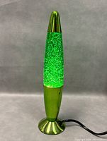 Full view of green lava lamp lit with glitter flowing inside, metallic green base and cap, cord visible.