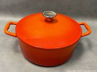Front angled view of orange cast iron pot with lid and handles on each side