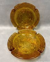 Close-up photo of a single amber glass ashtray showing concentric rings and cigarette rests in grooves around edges