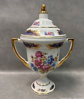 Photo of the porcelain covered urn with lid from a frontal angle showing floral patterns and gold embellishments.