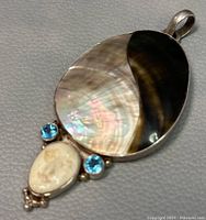 Front close-up of sterling silver pendant showing abalone and mother of pearl inlay with two blue gemstones and carved goddess face
