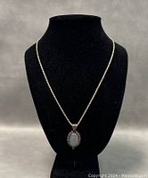 Front view of silver chain with light blue gemstone pendant displayed on black bust.