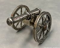 Side front view of the silver plated miniature cannon with visible ornate engravings on the barrel and wheels.