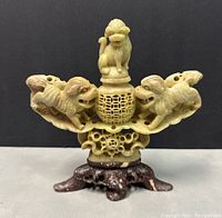 Front view of vintage hand carved soap stone incense burner with three Foo dogs around central lattice sphere and wooden style base.