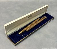 Two 18K gold laminated ballpoint pens displayed in a blue velvet lined Dynasty case with white cushioned top interior.