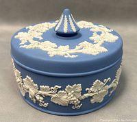 Front view of the closed light blue jasperware round trinket sweet dish showing white grapevine motif around sides and on lid with finial.