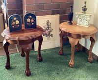 Two claw foot wooden tables with different stains, decorative bookends with floral inlay, framed botanical print behind, and two decorative objects on tables