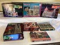 Overview of all 7 puzzles in the lot showing detailed boxes of famous architectural models and two 2D puzzles.