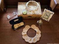 Overview of lot showing all items including white beaded collar, pearl collar, pocket watch, quartz clock, glasses in case, faceted glass perfume bottle, and glass curtain tiebacks