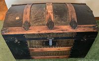 Front view of antique semi-dome trunk showing black and brown wood panels with snake skin textured design and metal latch lock.