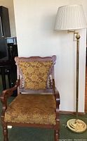 View of Victorian armchair with carved wood and floral upholstery next to brass standing lamp