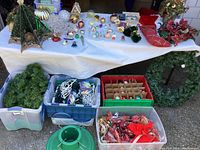 Photo of Christmas decorations laid on a table showing various ornaments, garlands and light strings stacked in and around plastic storage containers and boxes.