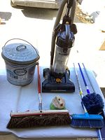 Eureka Powerspeed upright vacuum, metal Behr canister, various brooms and brushes on a table outdoors