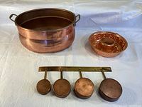 Photo showing large copper kettle, copper baking mould, and wall-mounted copper measuring cups on brass bar