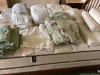 Top-down view of mattress with folded white sheets, green blanket, floral comforter, pillows and bolsters