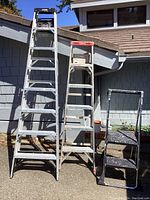 Photo showing three ladders side by side: Gorilla 8 ft ladder on the left, Werner 6 ft ladder in middle showing some wear, and black Cosco step stool on the right with three steps.