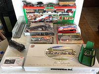 View of multiple boxed model train kits, assembled train cars, plastic train body, green tool set, and accessories arranged on a table showing the variety of model train related items.