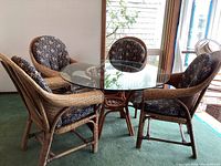 Overview of round glass tabletop on rattan pedestal base with four rattan armchairs and cushions