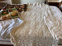 Five vintage crocheted items arranged on a bed including a large cream crocheted bedspread and smaller throws and cloths.