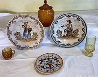 Photo showing the full set of two large painted bowls featuring a woman and a man, one small small decorative plate, and three amber glass items - a jar with lid, hobnail cup and goblet