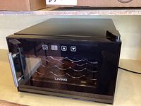 Front angle view of black Living wine chiller with glass door and control panel on top side featuring digital display and buttons.