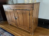 Front angled view of antique dry sink cabinet showing wooden paneled doors, white porcelain knobs, and natural wood grain.